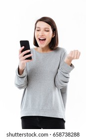 Picture of happy young caucasian woman standing isolated over white wall. Looking aside chatting by phone make winner gesture. - Shutterstock ID 658738288
