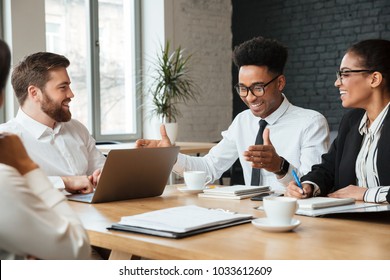 Picture of happy young colleagues indoors coworking. Looking at each other using laptop computer. - Shutterstock ID 1033612609