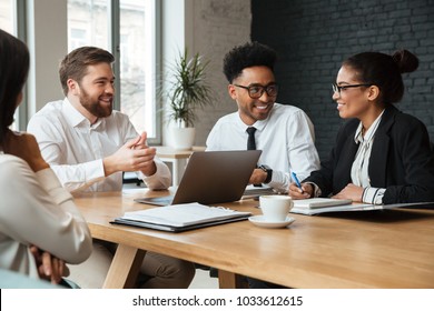 Picture of happy young colleagues indoors coworking. Looking at each other using laptop computer. - Shutterstock ID 1033612615
