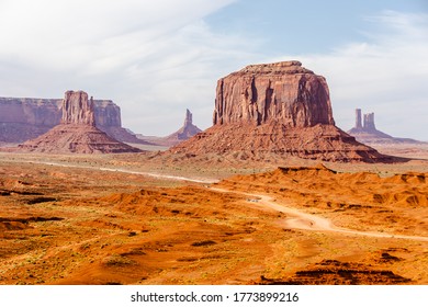 Picture Of Iconic Merrick Butte Rock Formation In Oljato-Monument Valley Taken On A Summer Cloudy Day From John Ford's Point. The Scenic Drive Dirt Road With Tourist Cars Winds Through The Red Sand.