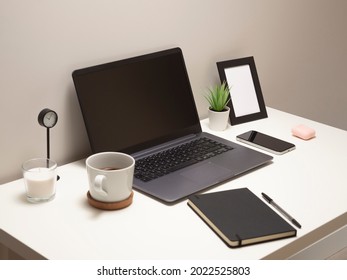 Picture Of Laptop On A White Table With A Mug A Clock A Small Bush A Notebook A Phone A Picture Frame And A Headphone Case