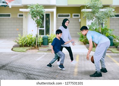 Picture Of A Little Boy Playing Basketball With His Parents In The Driveway