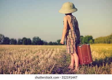 Picture of little boy wearing pith helmet and plaid romper carrying big valize in countryside . Kid in safari hat looking back on the blue sky outdoors background - Shutterstock ID 312191447