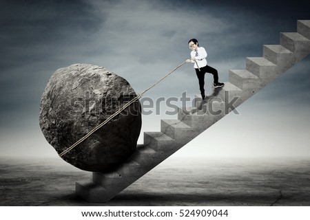 Picture of a little businessman climbing up a stairs while dragging a big stone. Concept of difficulty and persistence