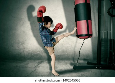 Picture Of A Little Child Wearing Boxing Gloves While Kicking A Boxing Sack