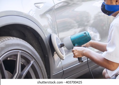 Picture of a male worker polishing a silver car body with an auto polisher machine