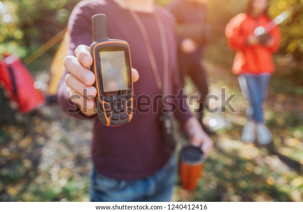 Picture of\
man holding satellite phone and thermocup in hands. He shows it to\
camera. Young man and woman stand\
behind.