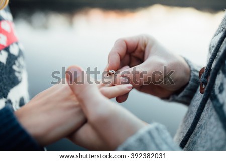 Picture of man putting engagement silver ring on woman hand, outdoor. Sea or river background.