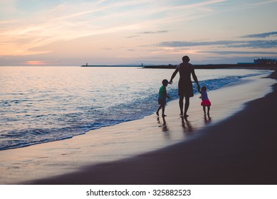 Picture Of Man Walking With Boy And Girl On Sunset Beach. Silhouette Of Happy Family Beside Seawaves On Dark Blue Seaside Outdoor Background.