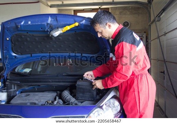 Picture of a mechanic in his workshop replacing a\
car battery. Maintenance\
works\
