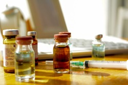 Picture Of A Medicine Bottle And Syringe On A Doctor's Desk That Is Exposed To Sunlight