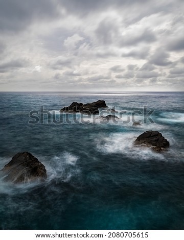 Picture of the Mediterranean Sea with dark blue water with three huge rocks, a cloudy sky and moving. 
