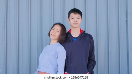 A Picture Of A Mother And A Teenage Son. Teenage Son Taller Than Mother Happy Family. The Background Is A Pattern Set From A Metal Container. An Asian Mother With Short Black Hair Looks Happy.