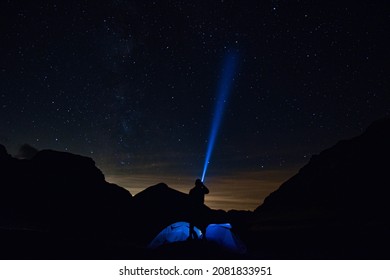 Picture of the nightsky with a person with a flashlight and a tent in the foreground. - Powered by Shutterstock