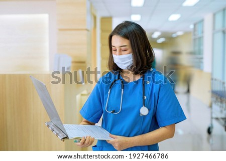 Picture of a nurse wearing a mask and opening a file for Read information about the patient, the patient in front of the corridor. Lobby in clinic hospital
