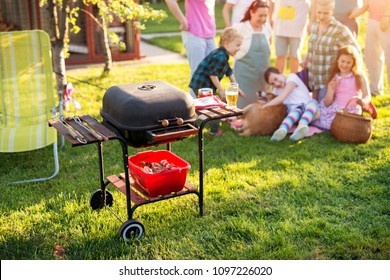 Picture Of Old Vintage In Good Shape Grill In A Yard With A Family Playing With A Dog In The Background.