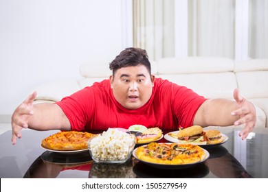 Picture of overweight man hugging at a lot of unhealthy food on the table. Shot at home