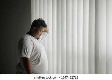 Picture of overweight man looks lonely while standing near the window in the dark room