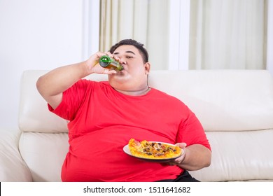 Picture of overweight man watching TV while eating pizza and drinking beer on the couch 
