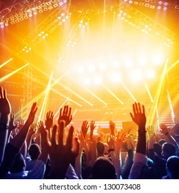 Picture Of A Lot Of People Enjoying Night Perfomance Of Famous Dj, Large Crowd Of Youth Dancing With Raised Up Hands On Rock Concert, Party In Dance Club, Bright Yellow Light From Stage, Nightlife