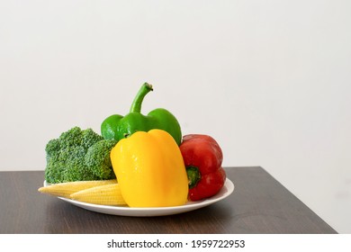 A picture of a plate full of exotic vegetables colourful vegetables including broccoli, baby corn, capsicum, red capsicum and yellow capsicum.