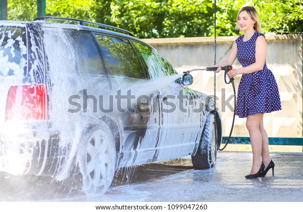 Picture, portrait of a young, smiling, attractive\
woman washing a car on a car wash, car wash, foam cleaning,\
pressure water