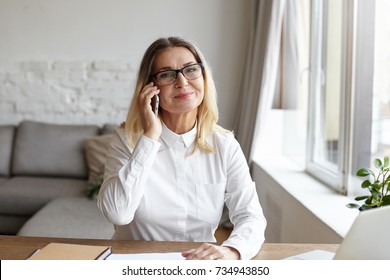 Picture Of Positive 60 Year Old Female Teacher Wearing White Blouse And Stylish Rectangular Glasses Smiling Joyfully While Talking On Smart Phone With Her Grandson During Working Day At University