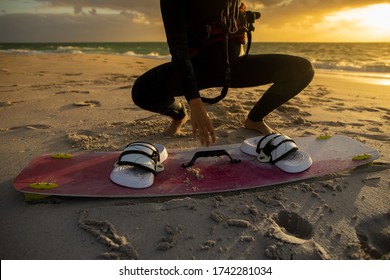Picture of professional female kitesurfer wearing a black wetsuit setting and picking up kitesurfing board equipment prior surfing sunsetting on the beach at the background   - Shutterstock ID 1742281034