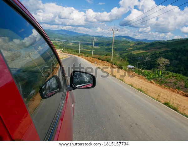 Picture of a red car on\
a road along the river, in contact area of ​​Chiang Rai Province,\
Thailand and Laos.
