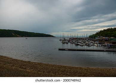 Picture of the sandy beach and bay with docked boats under an overcast grey sky