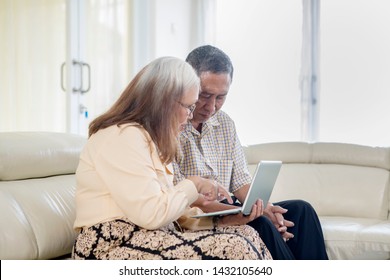 Picture of senior couple using a laptop computer together at home while sitting on the sofa - Shutterstock ID 1432105640