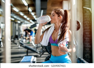 Picture Of Sexy Fit Girl Sitting In A Bight Gym And Drinking Water. Listening To The Music And Resting After Training,