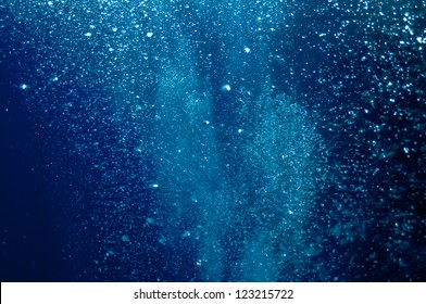 The picture shows underwater bubbles which raise from the depth blue sea