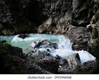 The picture shows a view of a raging river. This flows through stones and a stone wall. The river has beautiful light blue clear water.