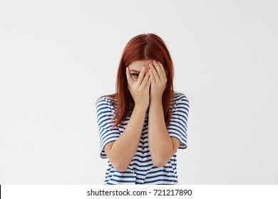 Picture of shy timid teenage girl with colored hair covering face with hands and peeping through her fingers at camera. Young woman hiding her face being frightened, scared or ashamed. Body language