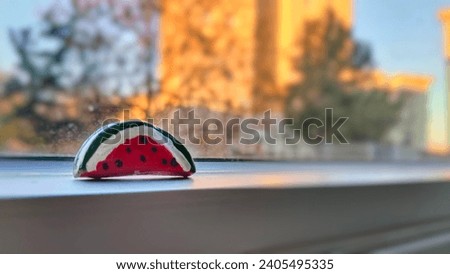 Picture of a small pin in the shape of a watermelon slice symbolizing Palestine with a blurred window background