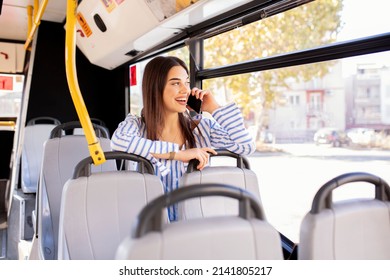 Picture Of Smiling Girl Sitting In Bus. Female Is Using Mobile Phone While Commuting By Public Transport. She Is Wearing Blue T Shirt.