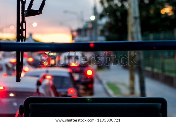 Picture taken\
from inside a bus, during peak hour, in the background can be seen\
traffic and the sunset, out of\
focus.