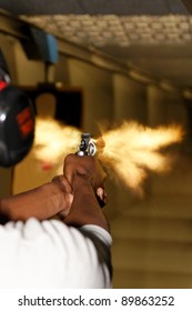 A Picture Taken Over The Shoulder Of A Young Man Firing A Gun At A Shooting Range In The Precise Moment Of The Muzzle Flash.