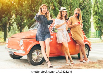 Picture of three beautiful girls best friends leaning on vintage car using smartphones and listening to music with headphones - technology and travel in Italy concept