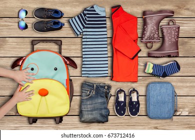 A Picture Of Travel Inventory Of A Child And Personal Belongings Clothes, Shoes, Sunglasses, A Cosmetic Pouch And A Child`s Hands Moving A Suitcase.