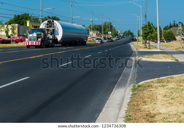 Picture of truck pulling oversize load of a big\
cylinder on black\
pavement