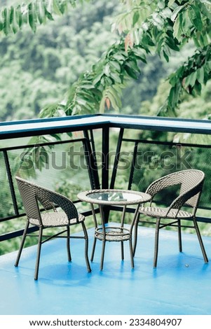 It is a picture of two chairs and a table located at the edge of the coffee shop's balcony. surrounded by trees and nature