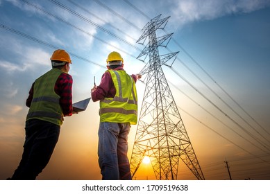 Picture of two electrical engineers using a notebook computer standing at a power station to view the planning work by producing electrical energy at high voltage electrodes. - Shutterstock ID 1709519638