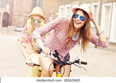 A picture of two girl friends riding a tandem bicycle in the city - Powered by Shutterstock