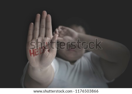 Picture of unhappy obese woman showing help word on her palm. Shot at black background