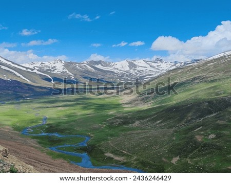 picture of a valley with snow covered mountains in background and a river flowing through