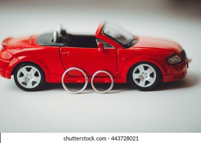 A Picture Of Wedding Rings Lying Behind A Red Toy Audi