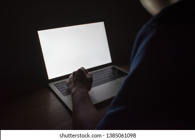 Picture of white light from a laptop on a wooden table in a dark room.