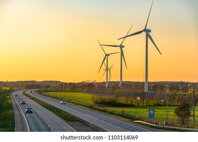 Picture Of Wind Farm Generators In The Green Field Close To The Road With Cars At The Sunset